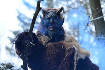 Teufelfigur im Winterwald. Mann mit geschnitzter Holzmaske mit Hörnern und teuflischem Grinsen...