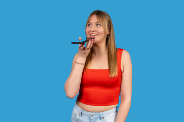 Young woman recording voice message on smartphone with blue background