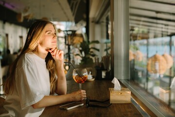 Young woman contemplating at a cafe window with drink in hand