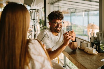Young man showing smartphone to friend in cafe