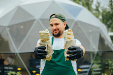 Man Offering Two Freshly Grilled Wraps at Outdoor Market