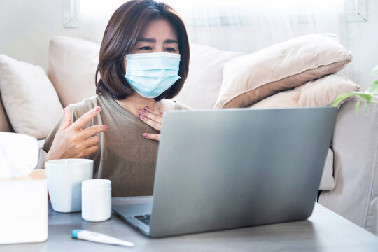 unwell Asian woman using laptop to video call doctor for online medical advice, consultation, diagnosis, and therapy concept of telemedicine and remote healthcare from home