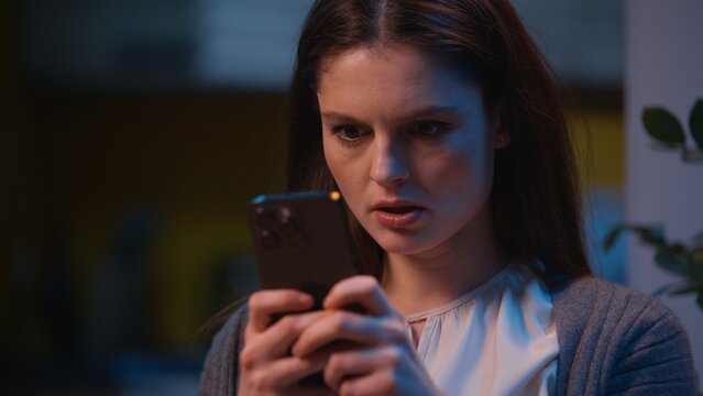 Angry woman irritated Caucasian girl texting message mobile phone chatting online social media chat messaging annoyed furious female using smartphone at night evening home negative emotions typing sms