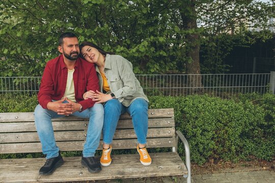 Happy couple sits on a bench outdoors, smiling and hugging each other. A joyful, affectionate moment capturing love, connection, and carefree togetherness in a relaxed, natural setting