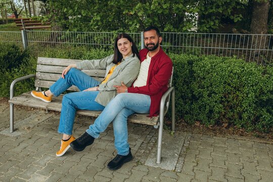 Interracial couple sits together on a park bench, smiling and enjoying a peaceful moment. A warm, loving connection capturing diversity, unity, and happiness in an outdoor setting