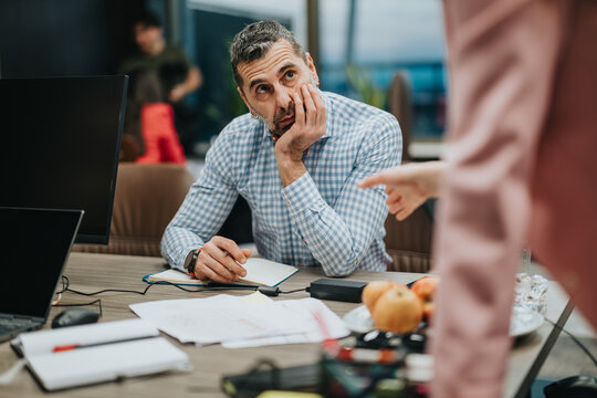 Businessman seated while attentively listening during an office interaction, reflecting on a subject with apparent concern and focus. The environment is professional, showcasing a modern workspace.