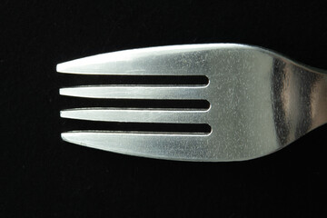 Macro photo of a silver metal fork on black background.