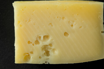 Close-up of a block of yellow cheese with holes, isolated on black background.