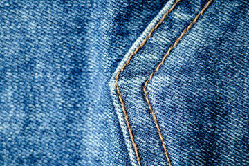 Close-up of blue denim fabric with double orange stitching detail.