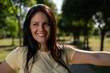 Beautiful fit woman stretching outdoors in park, athletic young female warming up before workout in natural green environment.