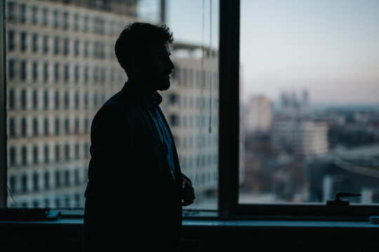 A silhouette of a professional standing before a large office window with an urban landscape in the background, creating an atmosphere of ambition, reflection, and city dynamics.