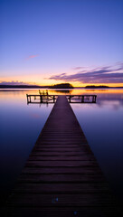 Fototapeta premium A tranquil sunset scene features a wooden dock extending into a calm lake with