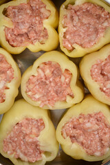 A close-up, overhead view shows several raw bell peppers, generously filled with a raw mixture of ground meat, rice, and onions, arranged tightly within a cooking pot
