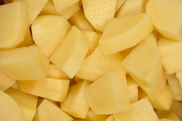 A close-up, overhead view displays a full frame of peeled and roughly chopped raw potatoes, ready...