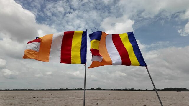 Two Colourful Buddhist Flags Waving in the Wind Against Cloudy Sky Over the Tien River Lien Hoa Pagoda, My Tho, Dong That, Vietnam