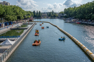 Naklejka premium Paris, France - 07 19 2025: Paris Beach, Bassin de la Villette. Detail view of pedalboats near the oudoor swiming pool and the instalations along the quays during Paris Beach in summer