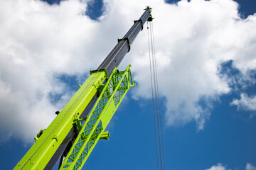 Construction crane reaching toward the sky illuminated by bright sunlight and fluffy white clouds
