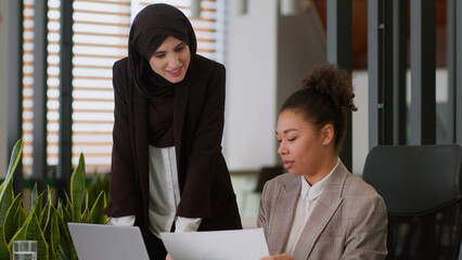 Two multiracial businesswomen female girls ethnic happy colleagues Muslim in hijab African American...
