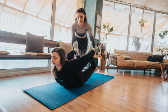 Two women engaged in partner yoga, assisting each other on a mat in a well-lit interior studio, emphasizing mindfulness, partnership, and physical wellness.