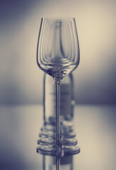Row of empty wine glasses and blurred bottle against  gray reflective background. Set of wine glasses. Shallow depth of  field. Toned image.