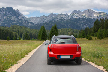 Montenegro, Durmitor National Park. Red SUV car on a road leading to the mountains on a summer day