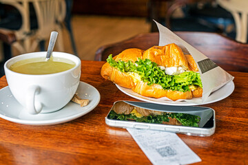 hot croissant with tuna, egg and salad near the phone with ginger tea. Lunch snack