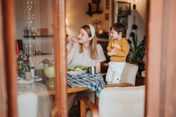 A mother and child share lunch in a comfortable home environment. The scene captures joy,...