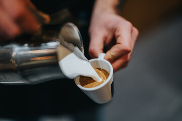 A close-up view of a barista creating latte art by skillfully pouring steamed milk into freshly brewed espresso in a white ceramic cup. Perfect depiction of coffee culture and artistry.