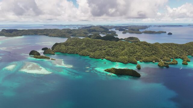 Sweeping drone shot revealing and showcasing the vivid aqua ocean and green-covered terrain off the coast of Palau. Wide revealing aerial drone shot.