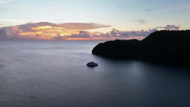 Breathtaking drone view scanning and revealing the sunset on the electric-blue seas and untouched islands in Palau. Cinematic view of Yacht in water.