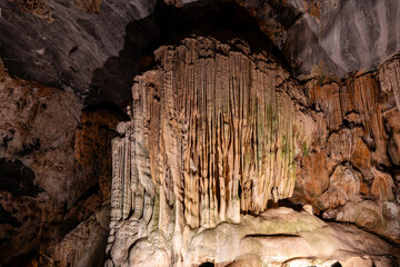 Eine imposante Nahaufnahme von Stalaktiten und Stalagmiten in einer Höhle, die durch künstliche Beleuchtung hervorgehoben werden. Die Felsformationen weisen verschiedene Texturen und Farbtöne von Beig