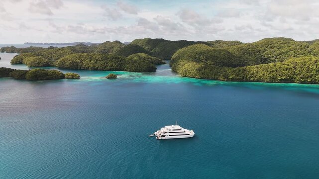 Aerial cinematic sequence gliding around the pristine turquoise sea and lush islets of Palau. Cinematic shot of a yacht in the lagoon.