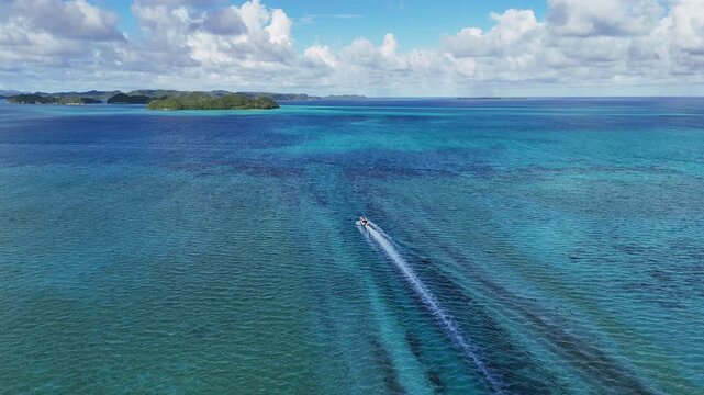 High-quality drone shot gliding around the glowing waters and emerald island dots surrounding Palau. Revealing drone shot of boat in the water.