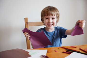 A five year old boy with blond hair plays and engages himself with colored paper. He is fooling...
