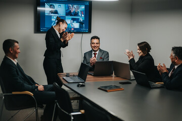 Corporate professionals gathered in a modern conference room engage in a discussion, clapping in...
