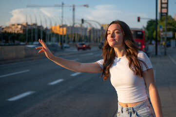 Young woman hailing taxi cab in city street at sunset
