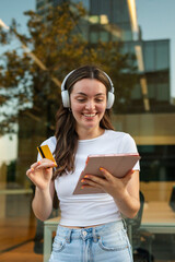 Young woman wearing headphones is shopping online using tablet and credit card