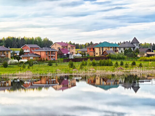 Reflection of colorful houses by serene lake in a tranquil rural landscape during early evening light