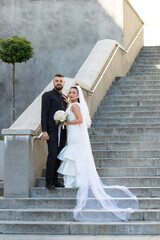 Bride and groom posing together on a stone staircase, the bride's long veil flowing down the steps....