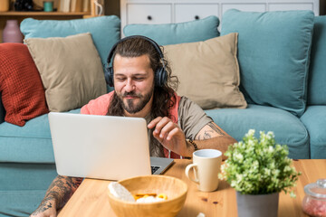 Young freelance businessman sitting on the floor in home office, working online on laptop computer, listening podcast or instruction, while earning the money on internet. Business independence concept