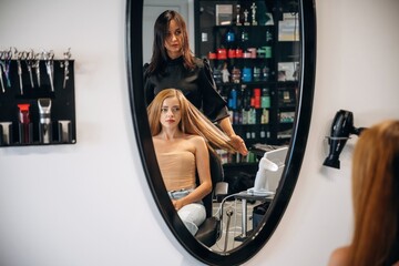 Customer is sitting on the chair. Woman is in a beauty salon with hair stylist