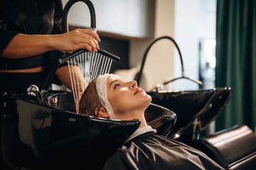Lying down, washing the hair. Woman is in a beauty salon with hair stylist
