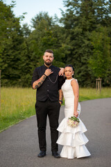 A wedding couple standing on an alley in a park. Bride in white dress with bouquet put her hand on...