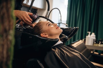 Service for customer, washing head. Woman is in a beauty salon with hair stylist
