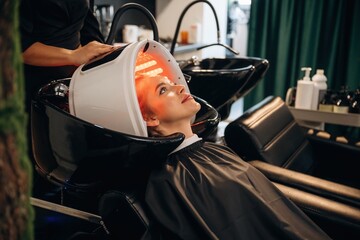 LED hair growth helmet. Woman is in a beauty salon with hair stylist