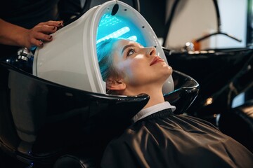 LED hair growth helmet. Woman is in a beauty salon with hair stylist