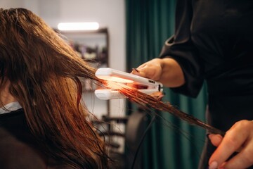 Straightening the hair. Woman is in a beauty salon with hair stylist