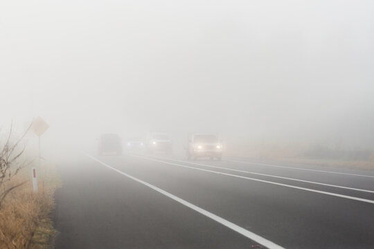 Cars travelling on highway road through fog with low visibility