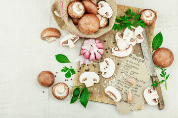 Rustic flat lay with fresh brown mushrooms, garlic, parsley, knife and handwritten recipe