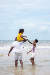 back view happy african family having fun on tropical seashore,father lifting a little daughter up...